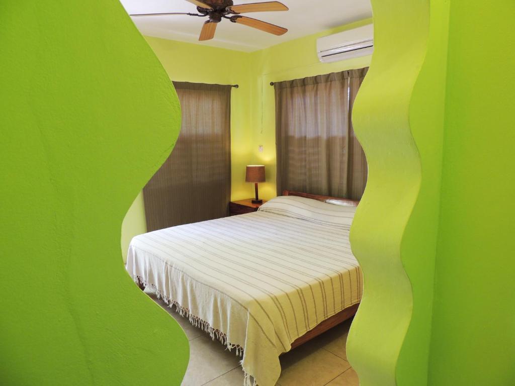Bedroom with bed, lamp, and curtains, viewed through green, wavy cutouts in a wall.