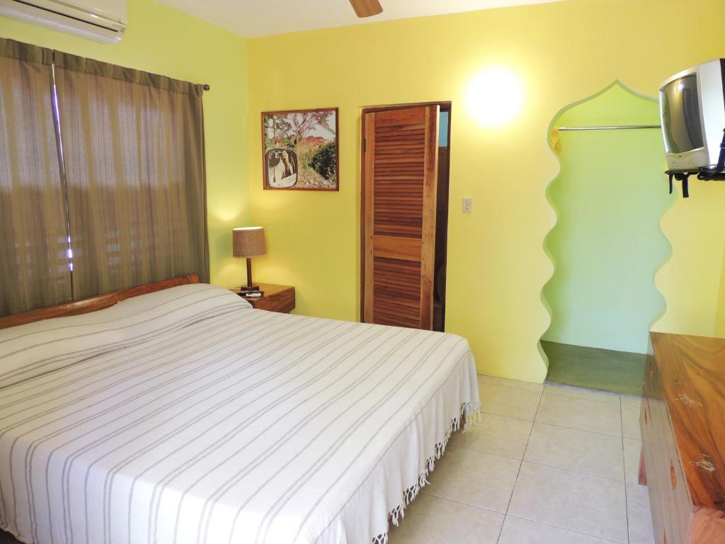 Bedroom with yellow walls, a bed, and a wooden closet. A TV hangs on the wall.
