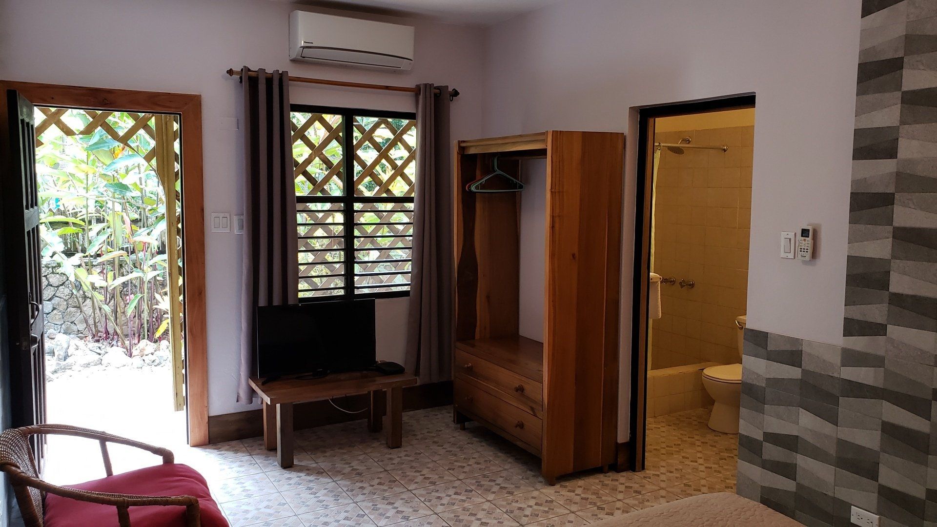Hotel room with open door to outside, TV, closet, bathroom doorway, and patterned walls.
