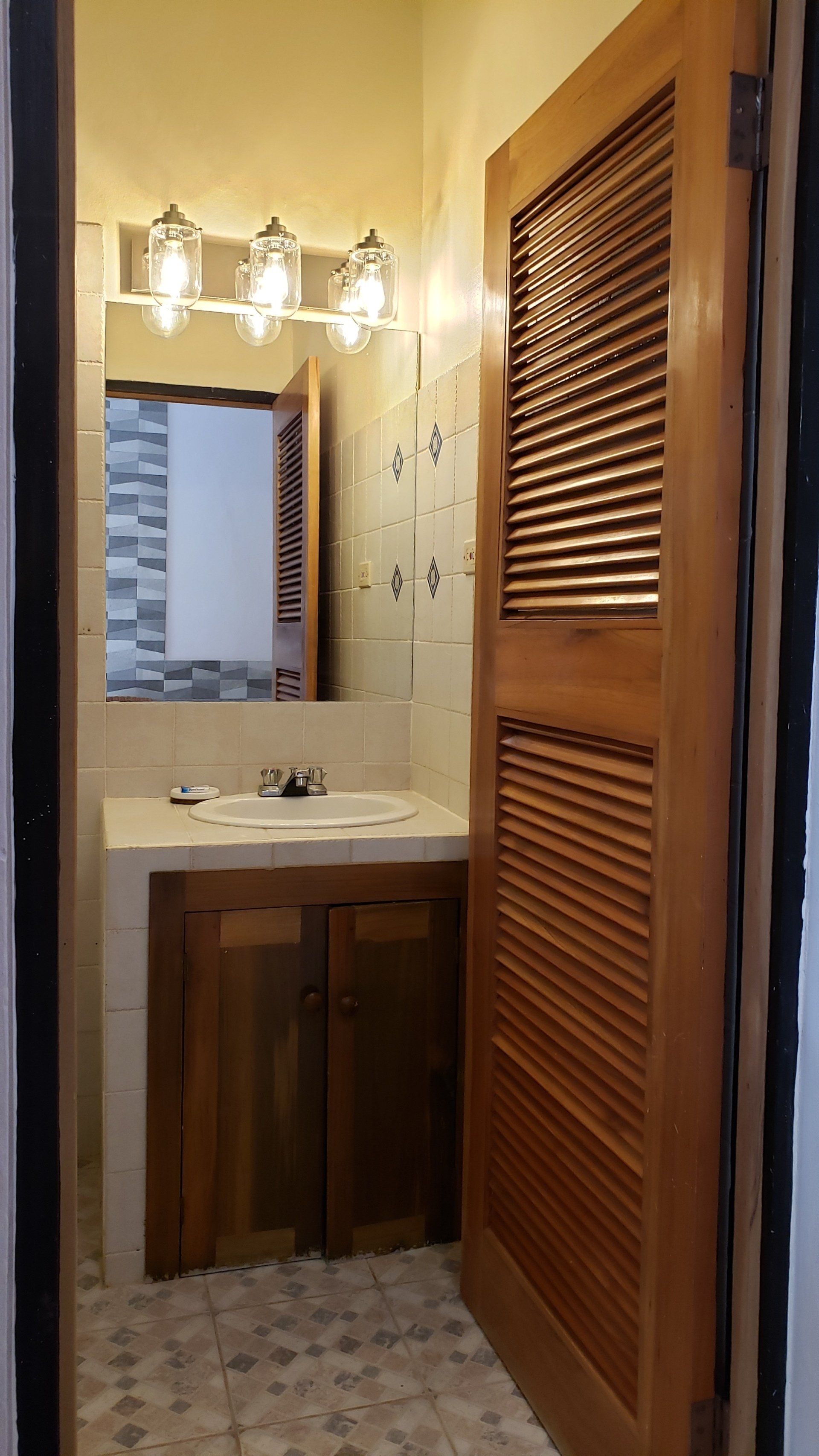 Bathroom with wooden door, vanity, and mirror; tile walls and floor.
