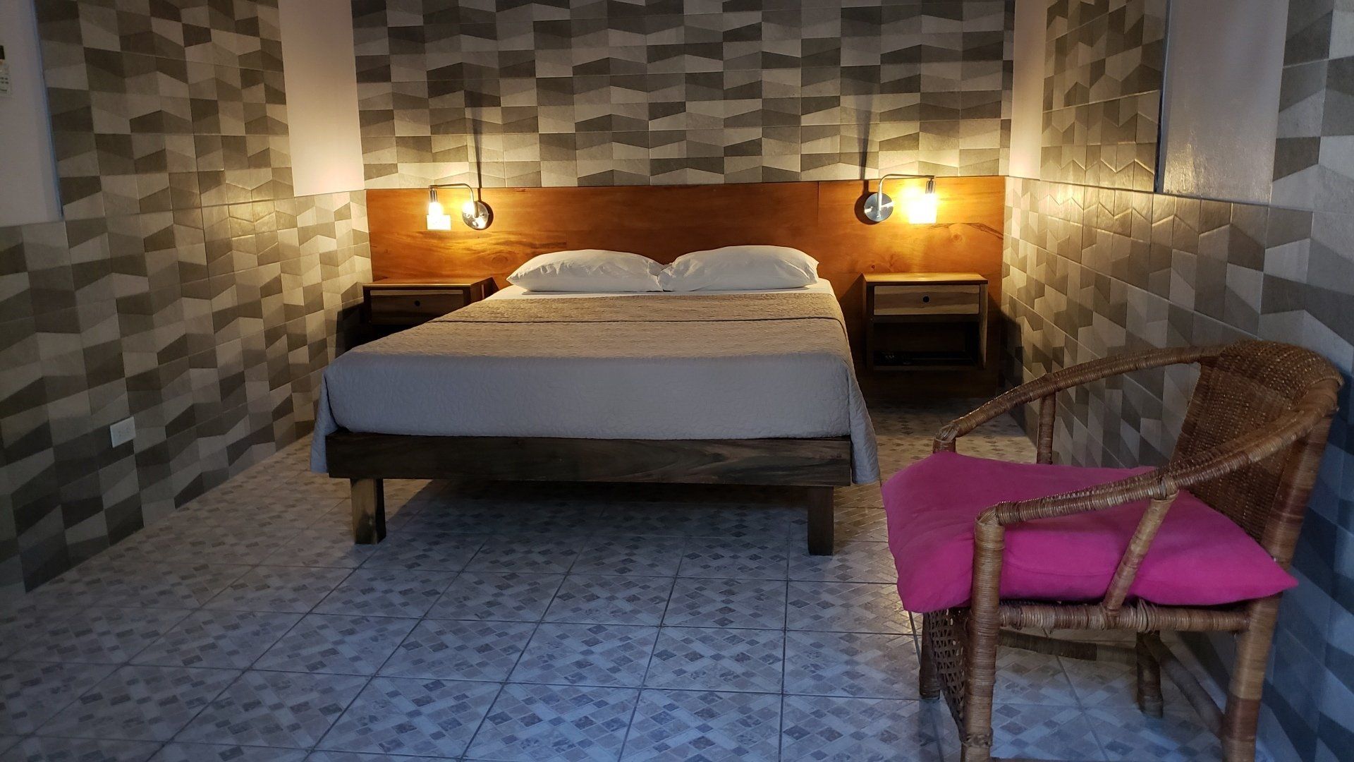 Bedroom with a bed, nightstands, chair, and patterned walls. Soft lighting.