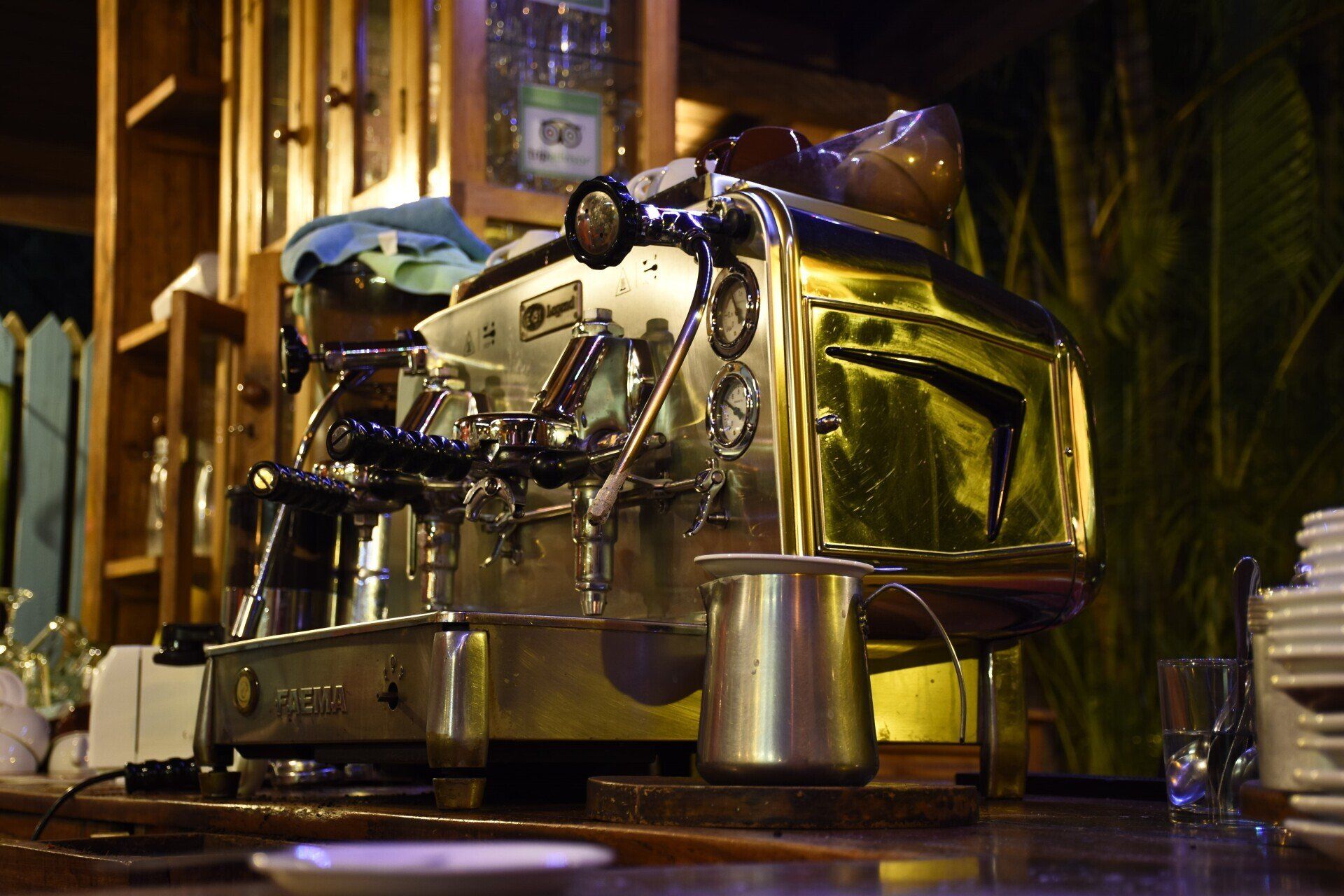 Shiny espresso machine on a wooden bar, in a cafe setting, with a small metal pitcher.