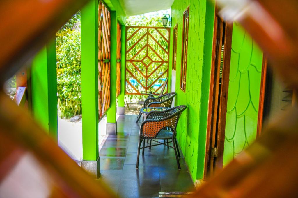 Green-walled porch with wicker chairs, framed by a wooden latticework; view from a diamond-shaped opening.