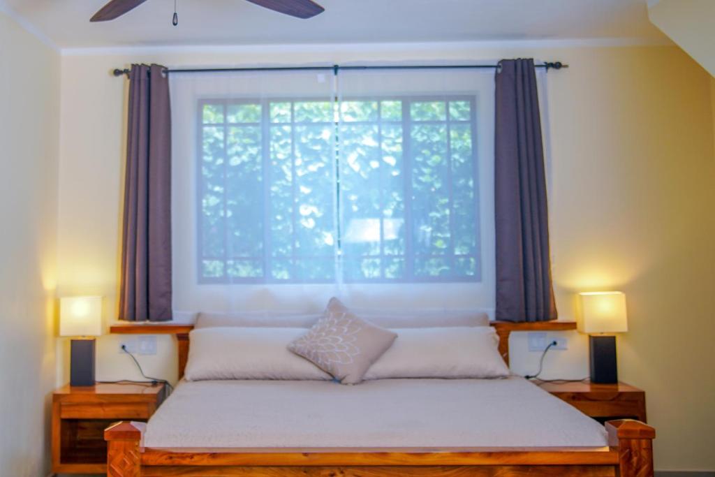 Bedroom with king-sized bed, window with sheer curtains, nightstands with lamps, and brown drapes.