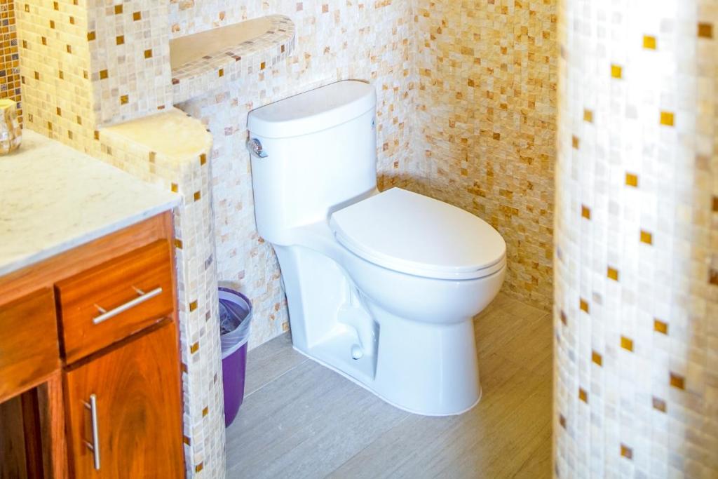 White toilet in a bathroom with mosaic tile walls and a wooden cabinet.