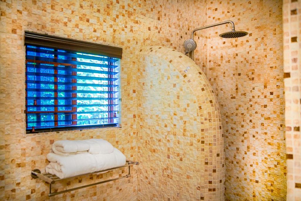 Mosaic-tiled shower with arched wall, window with blinds, towels on rack, and showerhead.