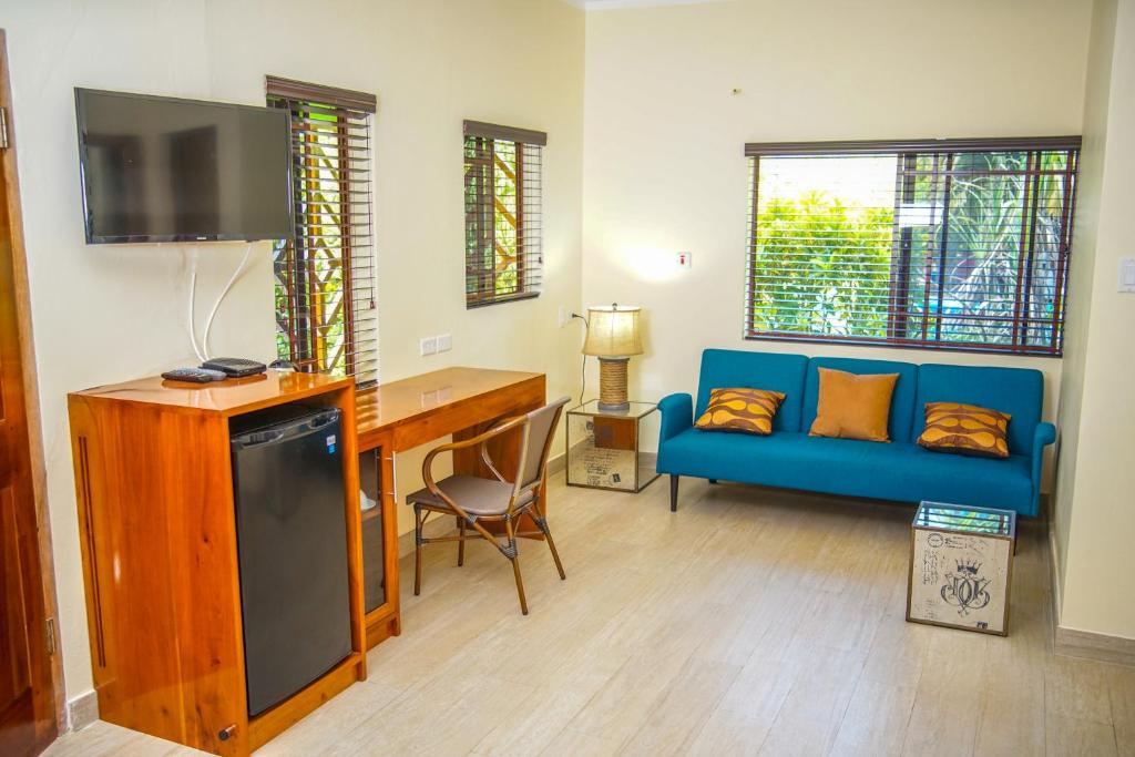 A furnished living space with a blue couch, desk, TV, and mini-fridge near windows.