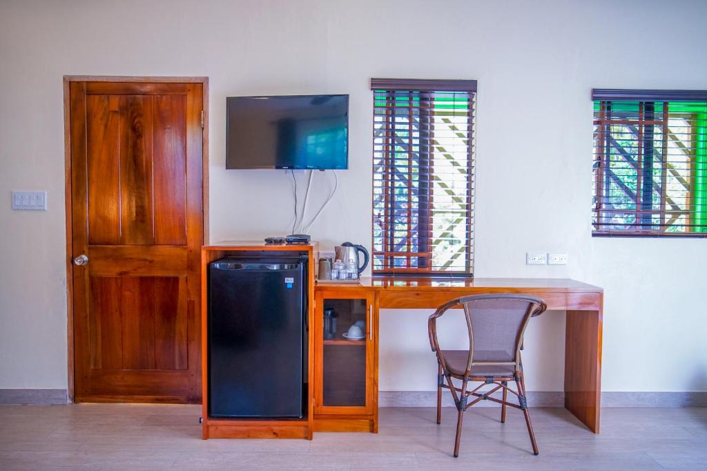 Hotel room with door, small TV, mini-fridge, desk, chair, and windows with colored glass.