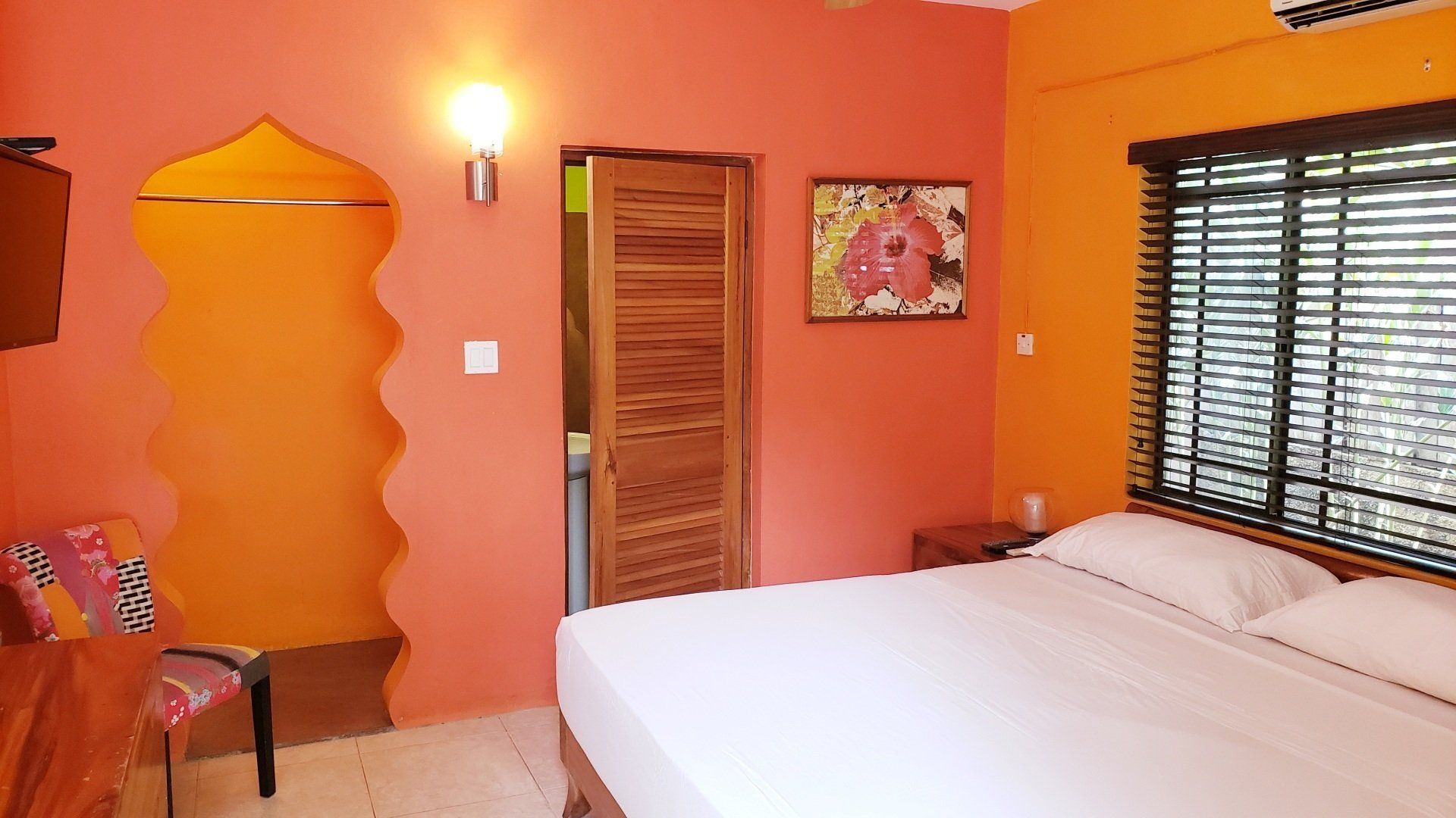 Orange and coral bedroom with a bed, artwork, and a window with blinds.
