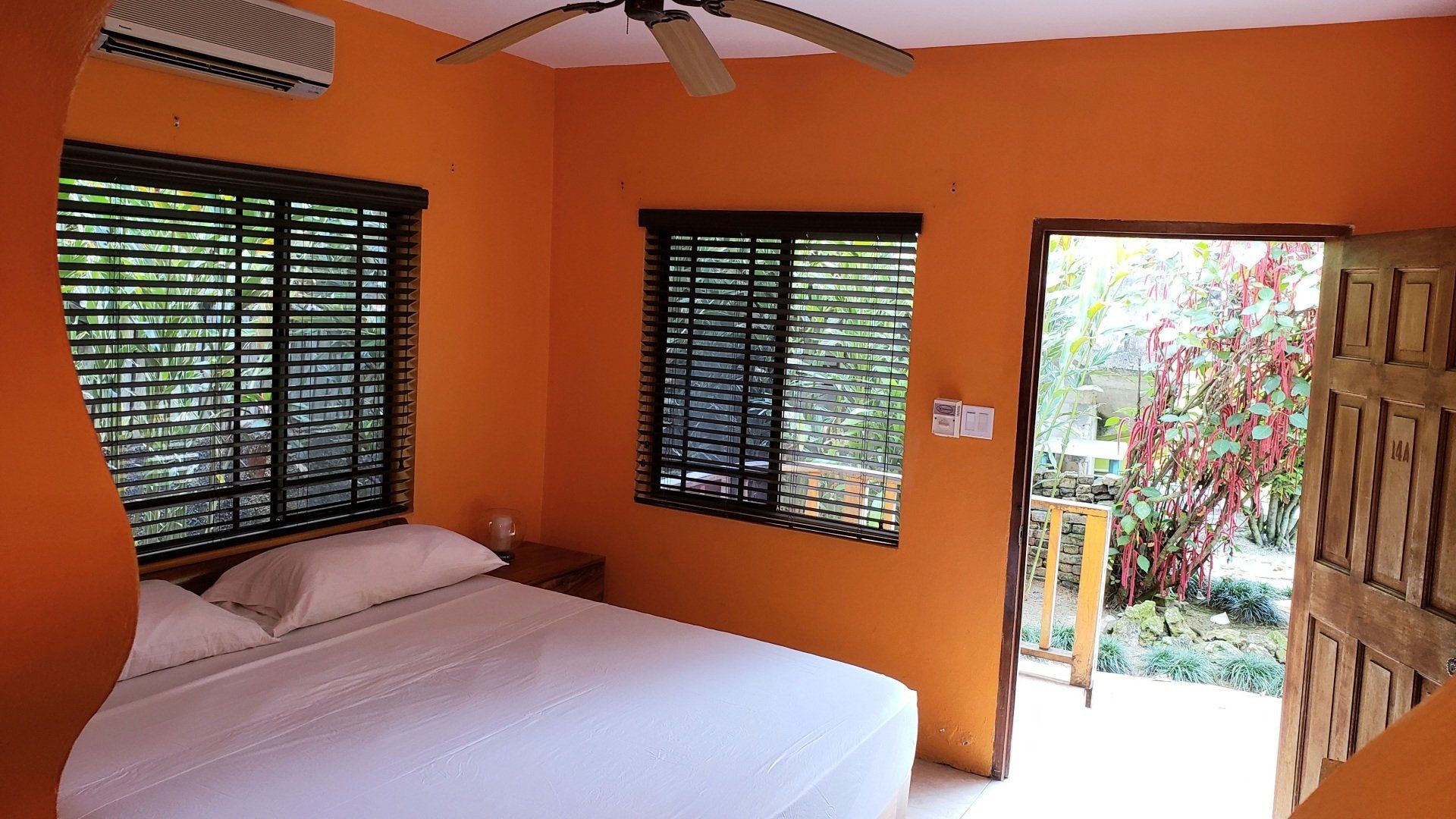 Orange-walled bedroom with a bed, windows, and an open doorway to a garden.