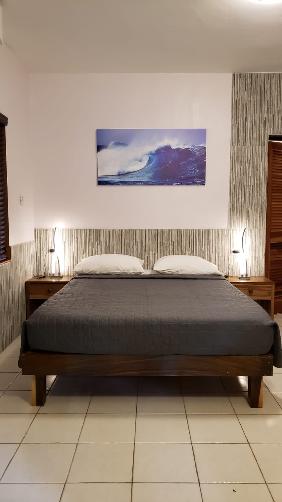 Bedroom with wooden bed, bedside tables, wave art, and gray bedding.
