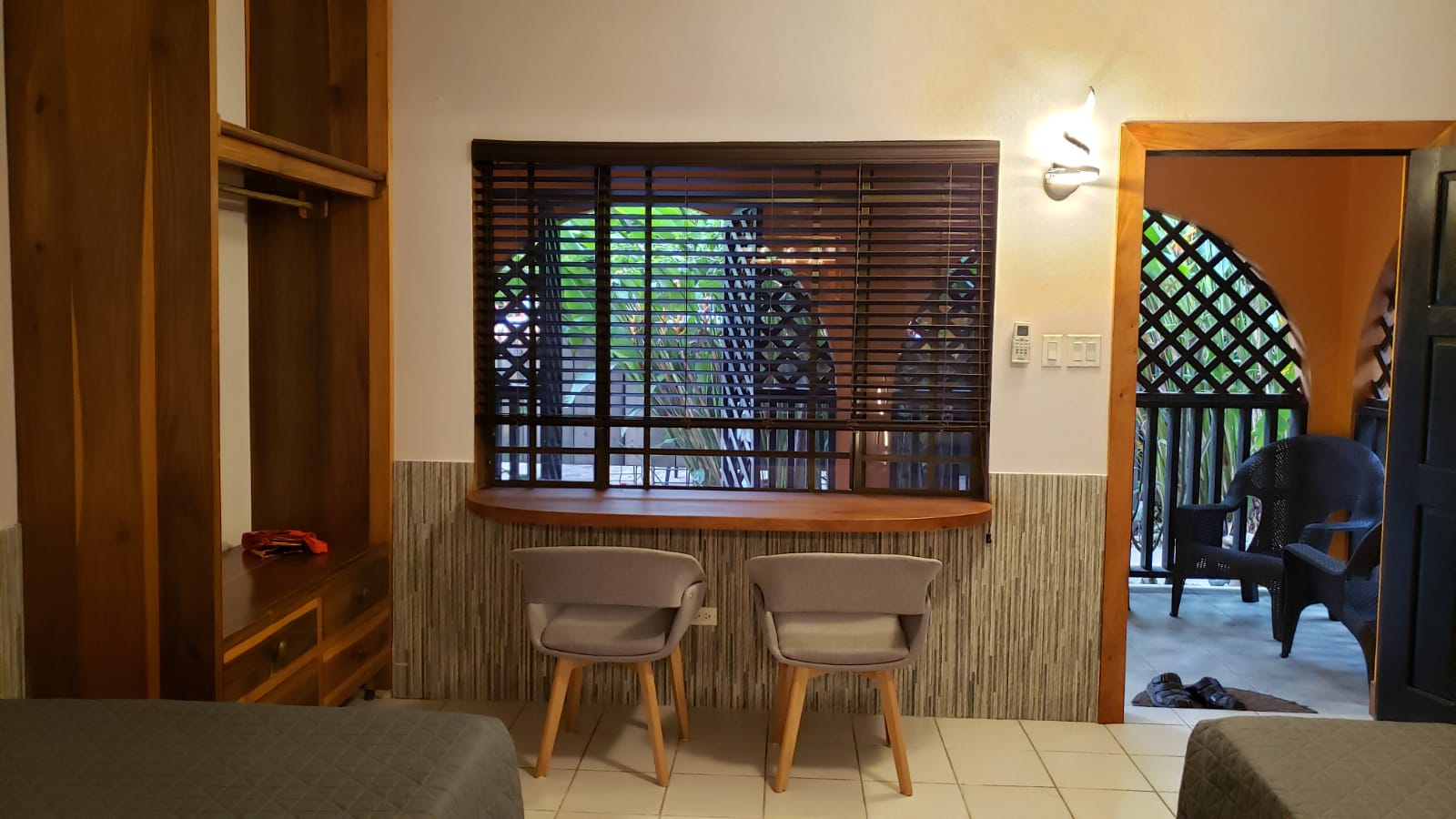 Room interior with wooden furniture, two chairs, window with blinds, and doorway to an outdoor space.