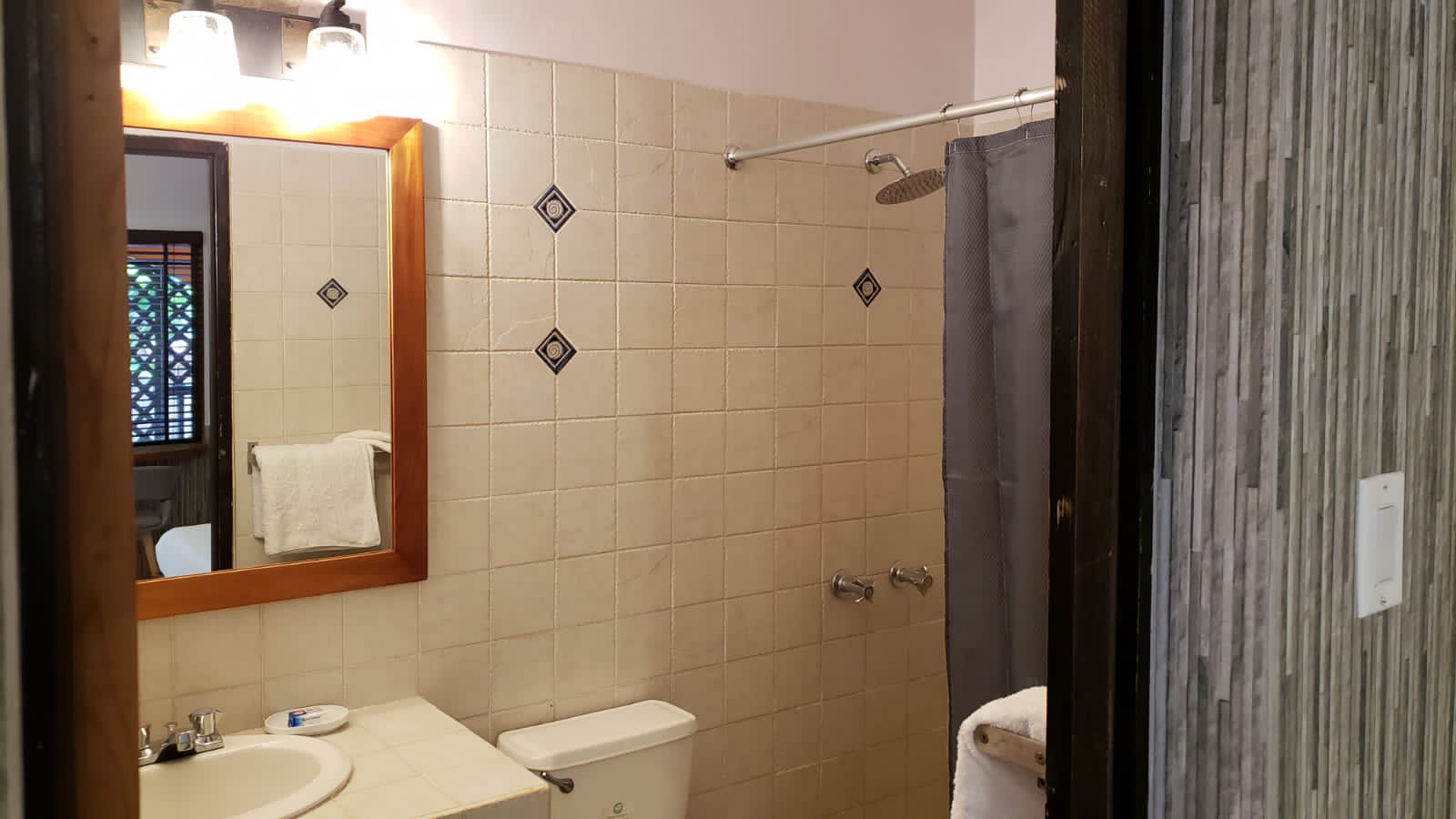 Bathroom with beige tile walls, a toilet, sink, mirror, and shower.