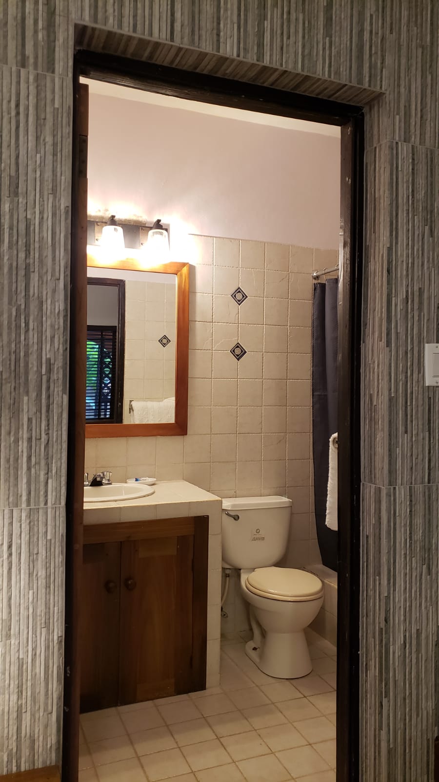 Bathroom with white tiles, toilet, sink, mirror, and a partially open doorway.