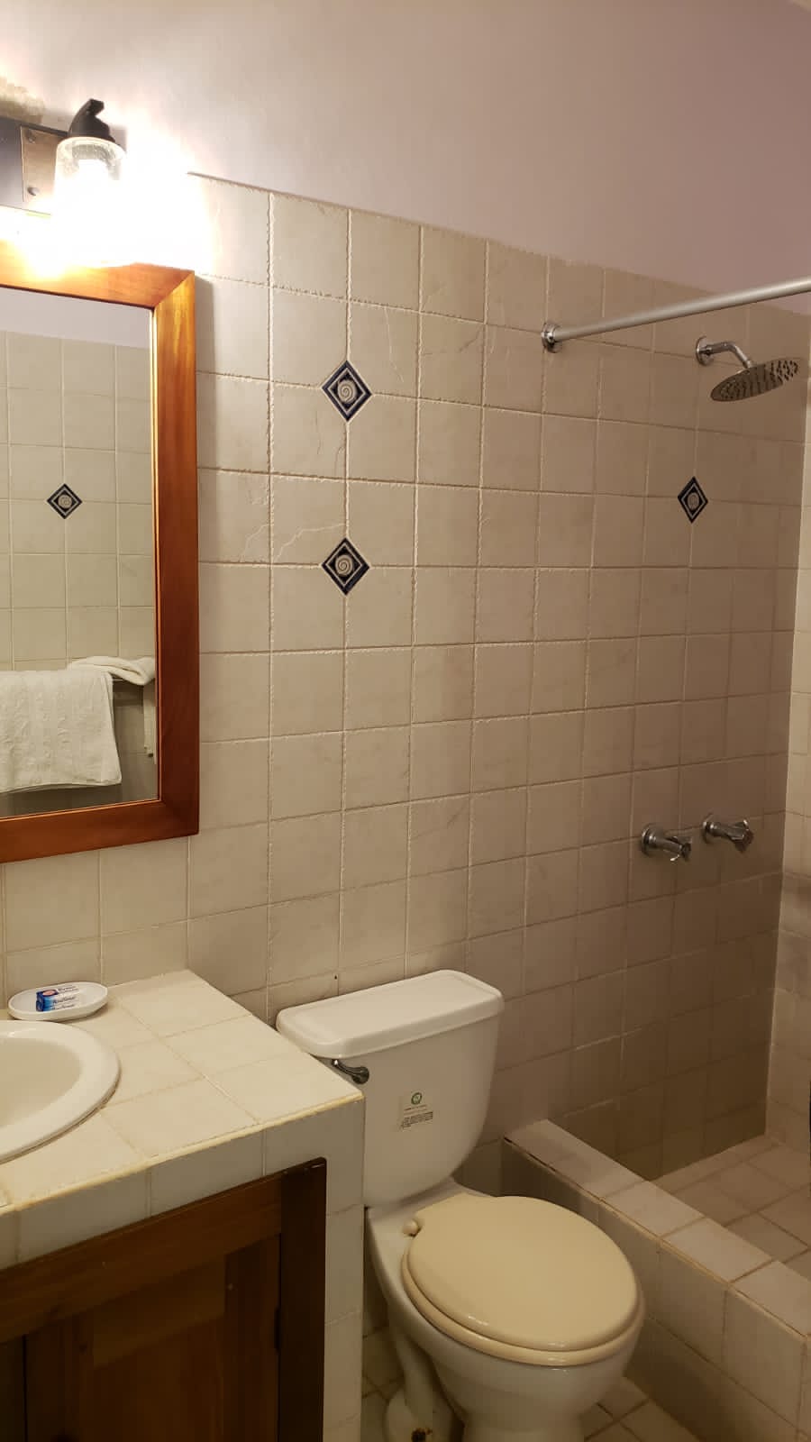Bathroom with white tile walls, a toilet, sink, mirror, and shower.