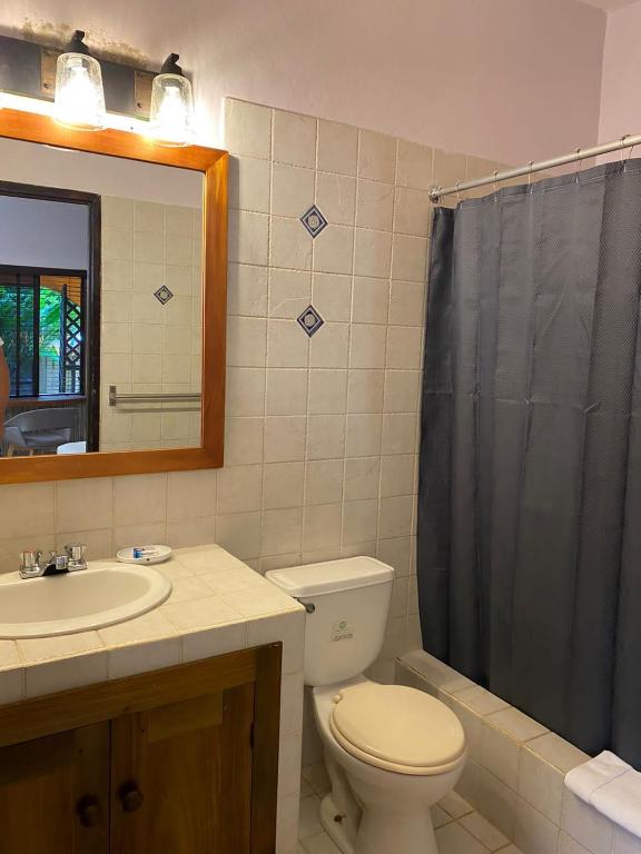 Bathroom with a sink, toilet, and bathtub with a gray shower curtain. Beige tiled walls.