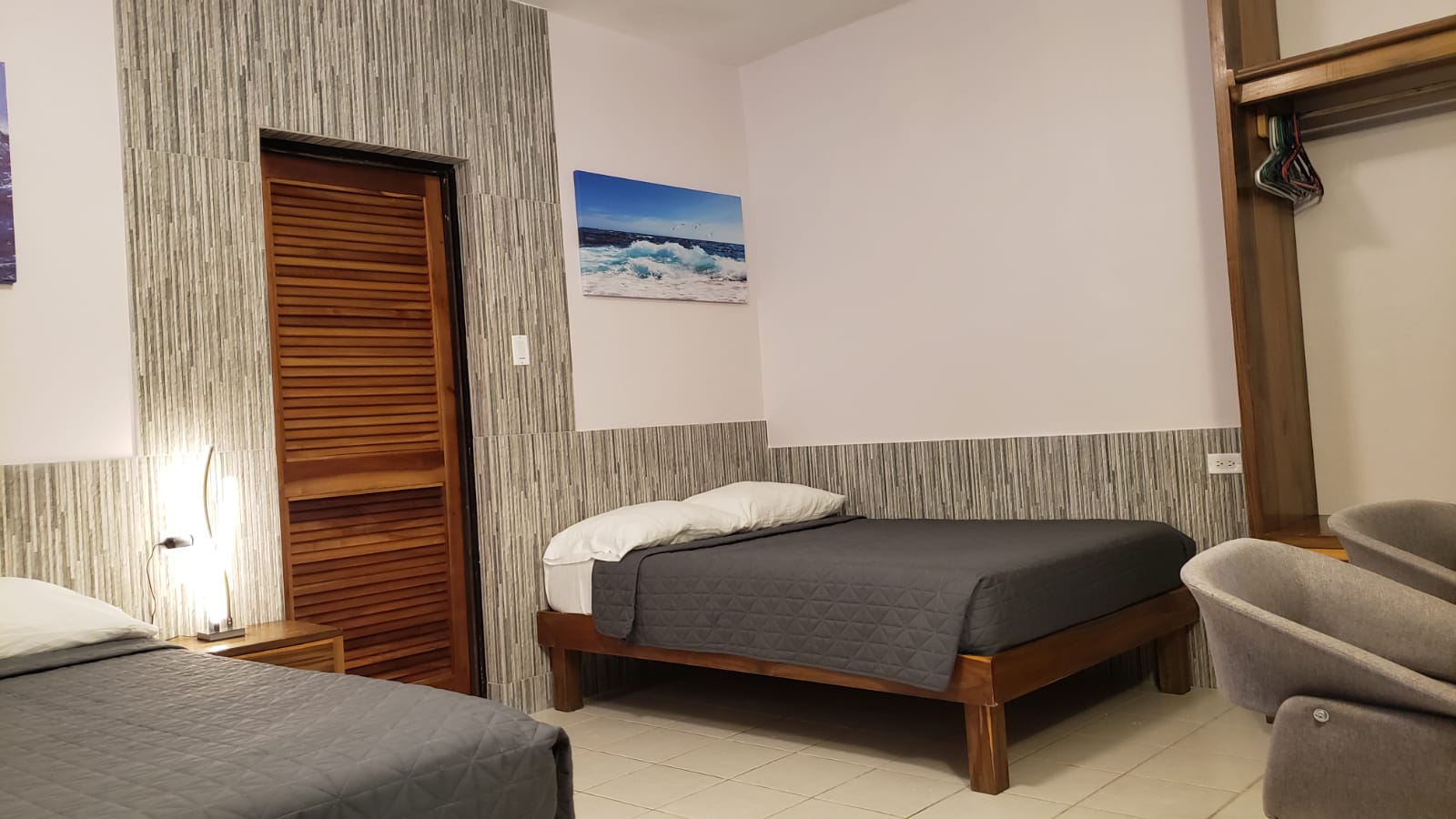 Bedroom with two beds, gray bedding, wooden frames. Walls are gray-striped, wooden door. Artwork of ocean.