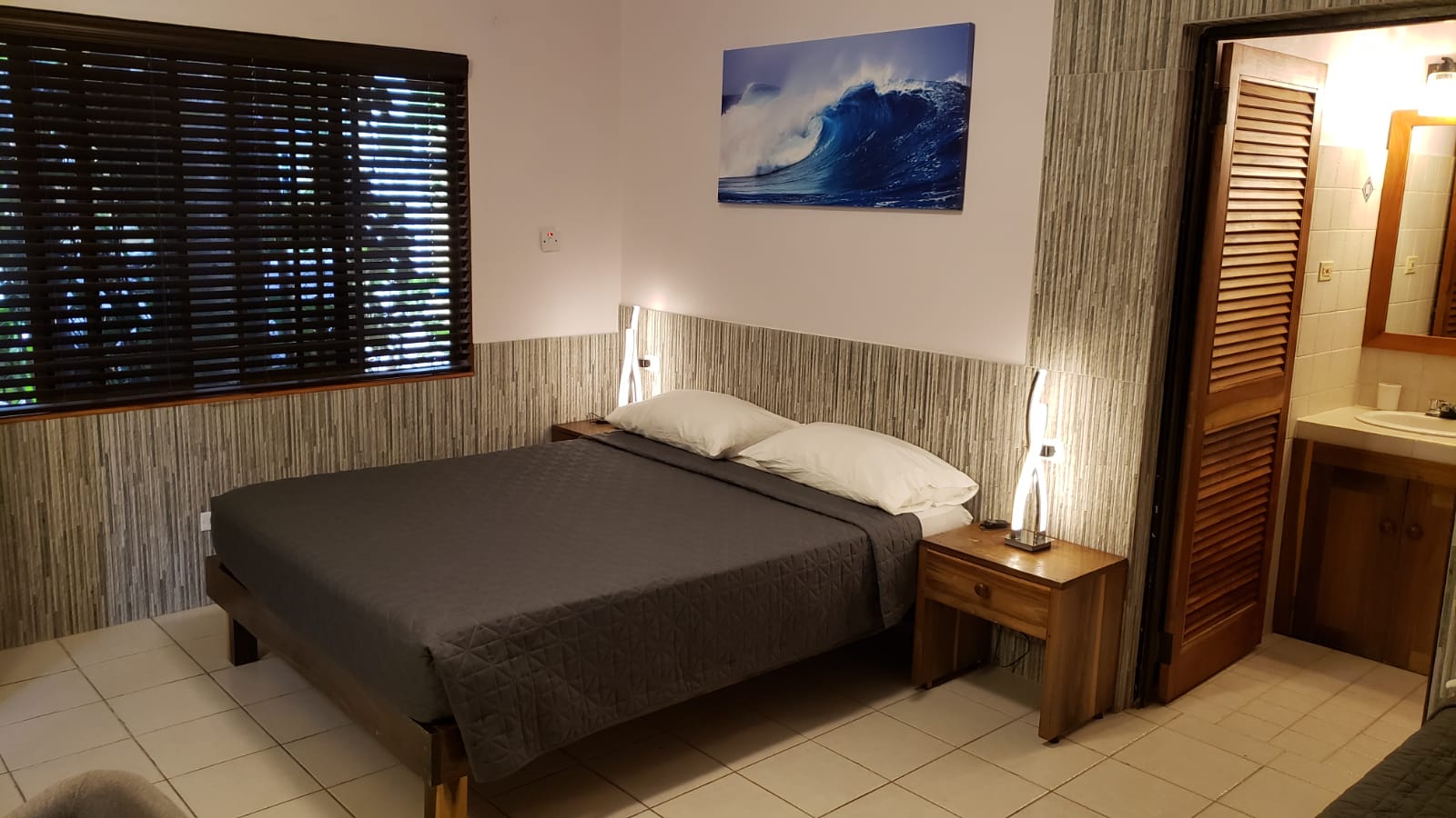 Bedroom with a bed, nightstand, window with blinds, and artwork of a wave.