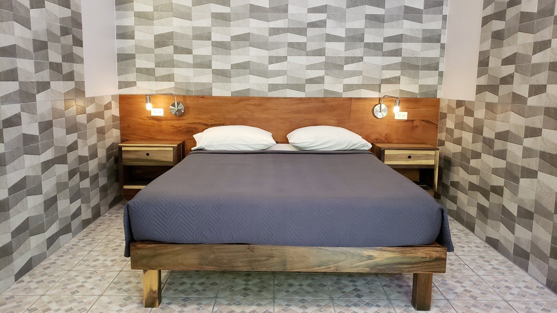 Bedroom with wooden bed frame, headboard, nightstands, and textured wallpaper.
