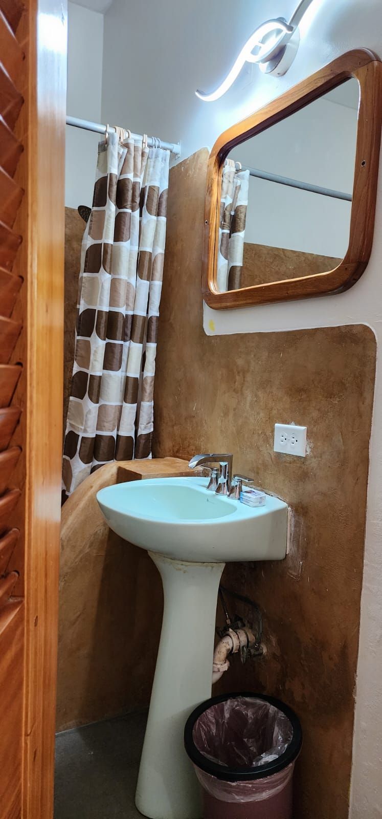 Bathroom with a pedestal sink, shower, and mirror. Brown and white patterned shower curtain and earthy walls.
