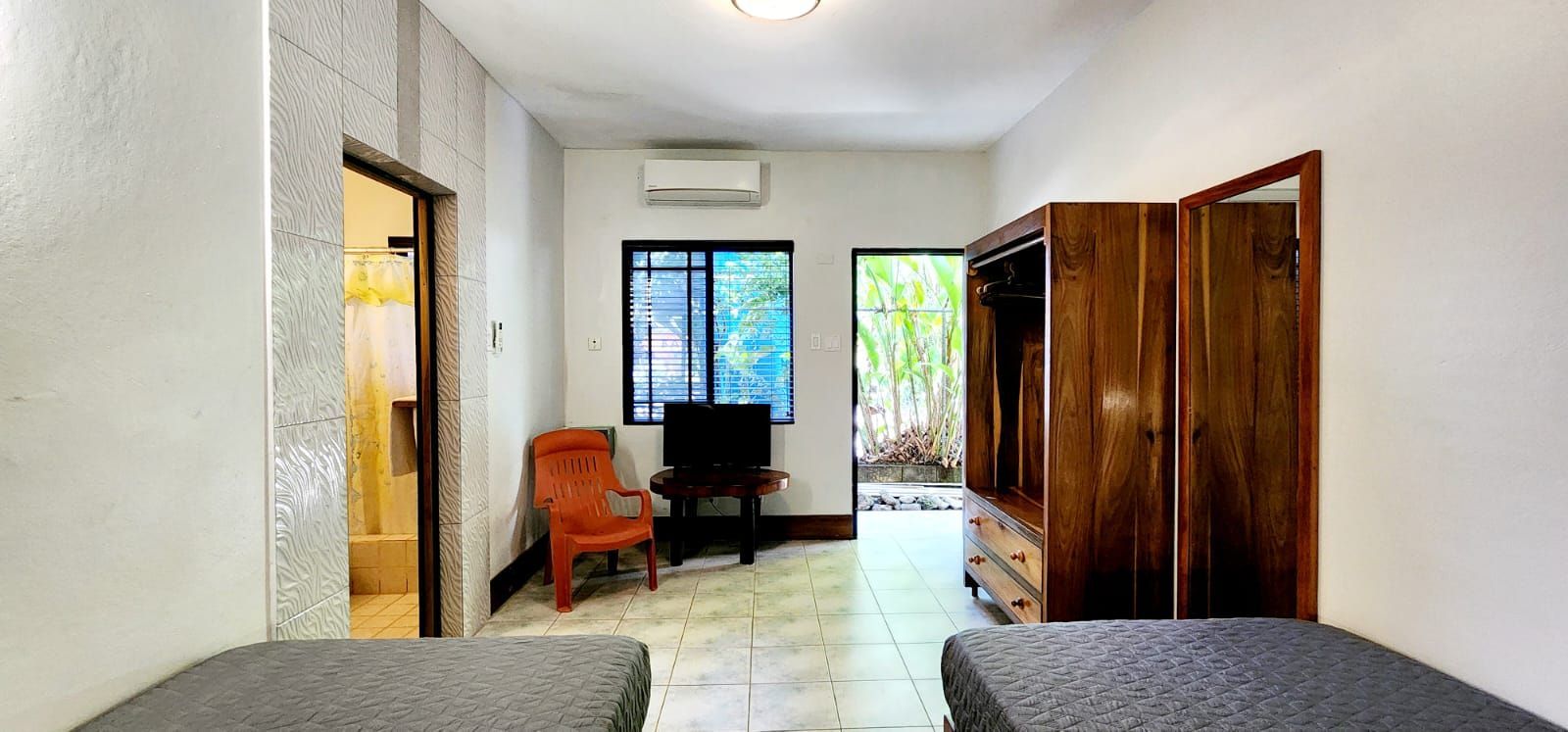 A room with a bed, wardrobe, TV, orange chair, and door leading outside.