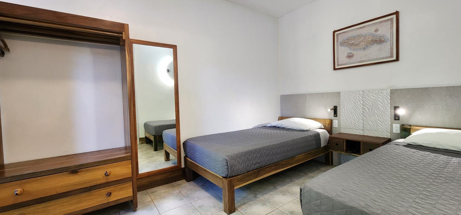 A small hotel room with two beds and a wooden wardrobe. A mirror is on the wall.