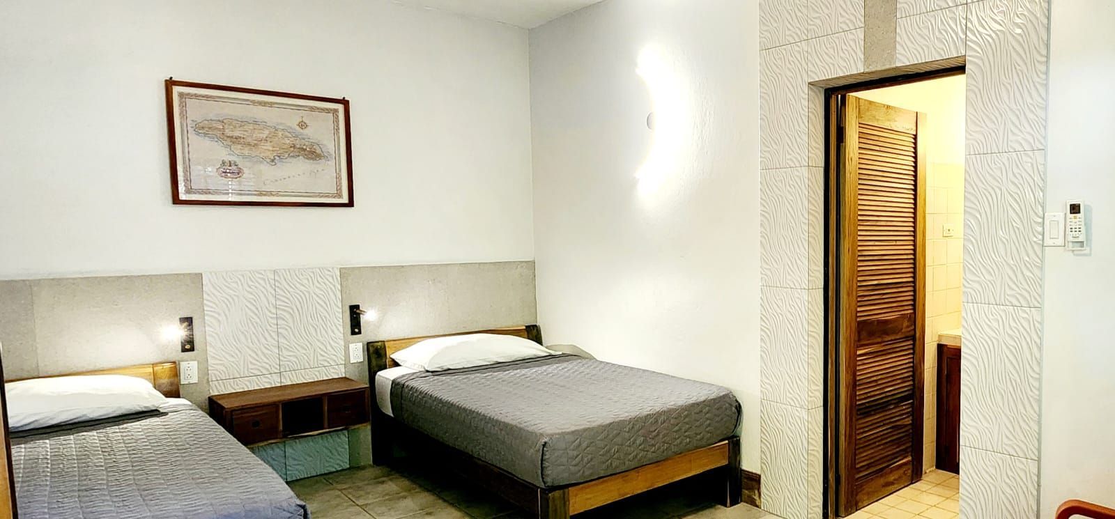 A hotel room with two beds, a map on the wall, and a door to a bathroom.