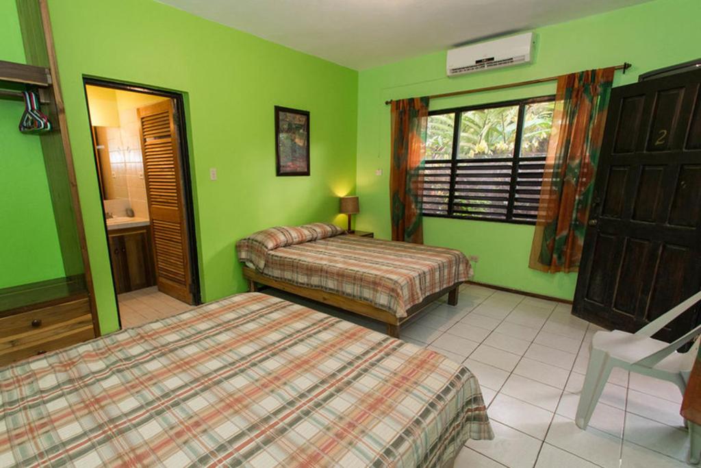 Green bedroom with two beds, window, open door to bathroom, air conditioning.
