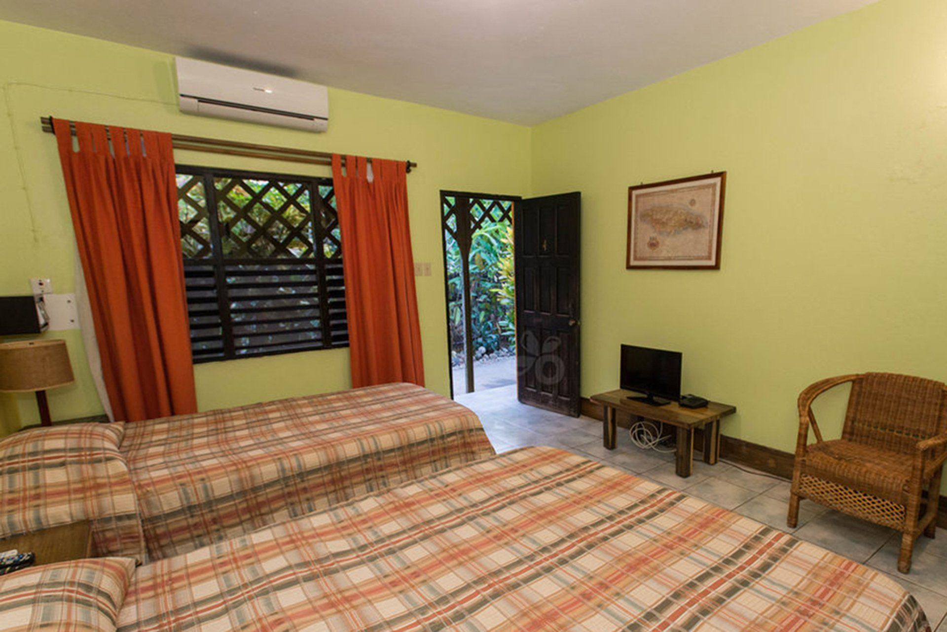 Two twin beds, orange curtains, and an open doorway to a garden.