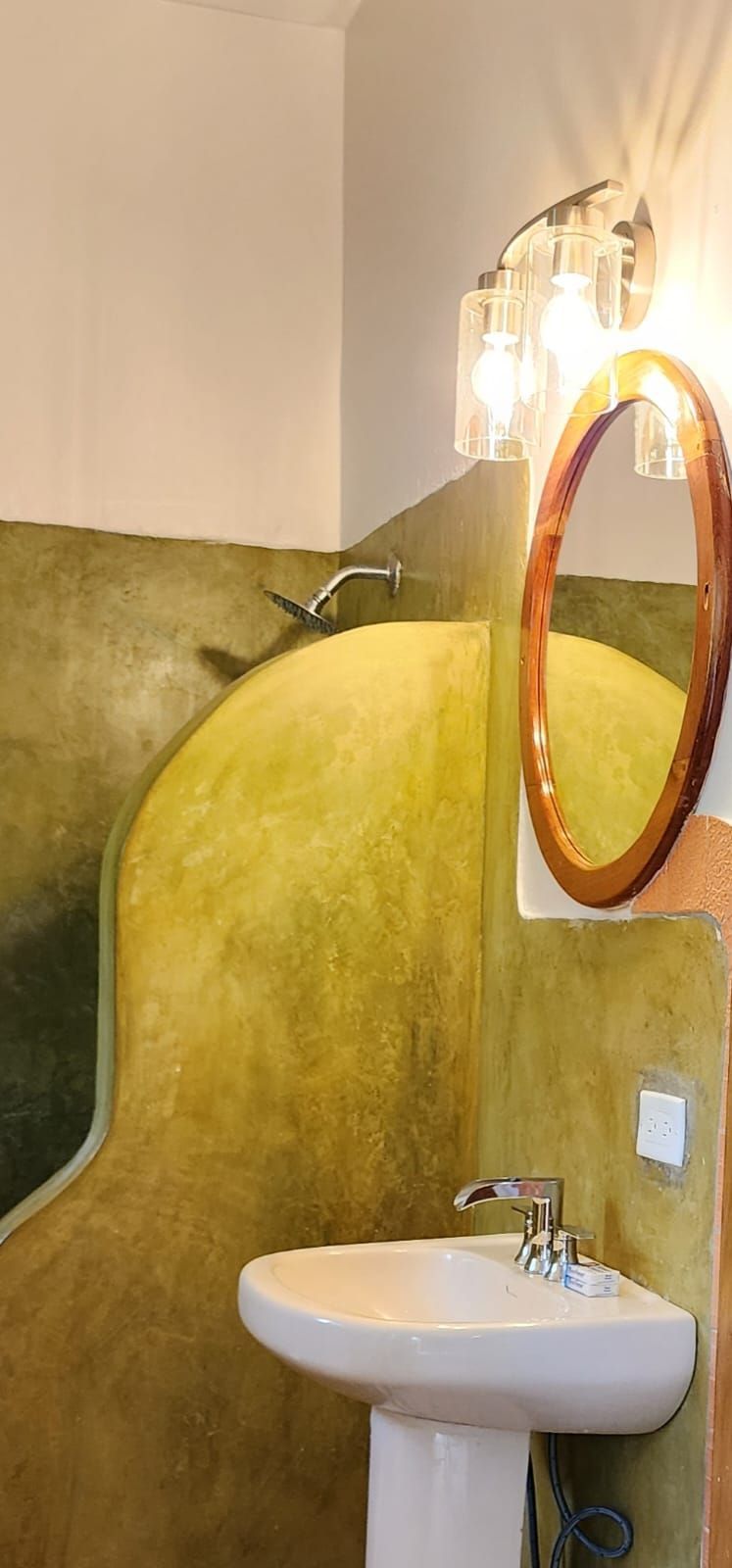 Bathroom with yellow textured wall, pedestal sink, and oval mirror.