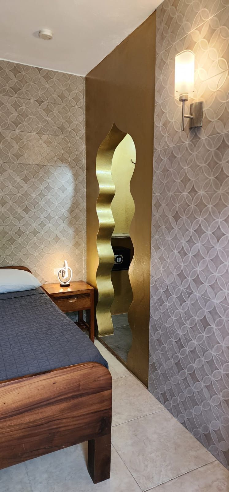A room with a wooden bed, patterned walls, and a golden arched doorway.
