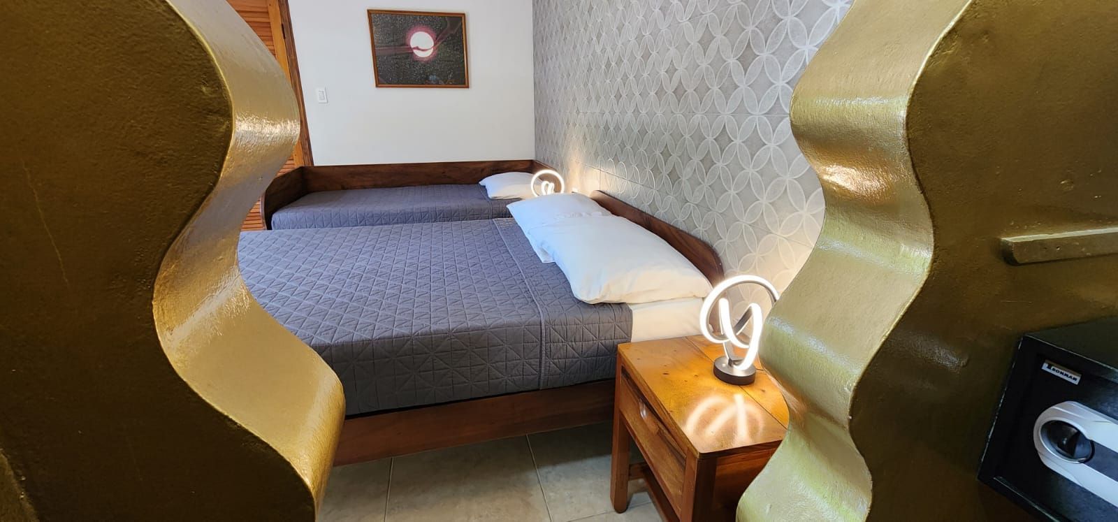 Bedroom with two beds, a bedside table, a modern lamp, and a framed artwork. 