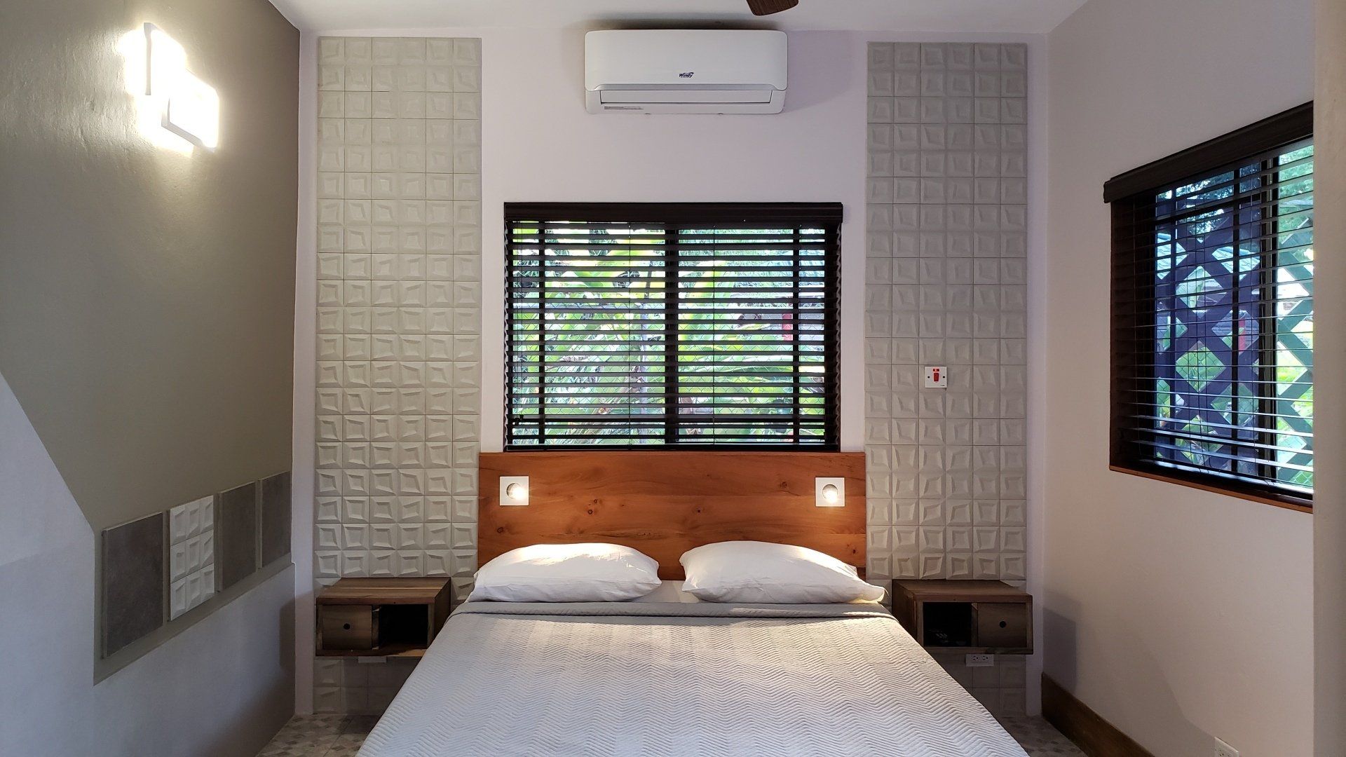 Bedroom with bed, nightstands, windows, textured wall behind bed, and air conditioner.