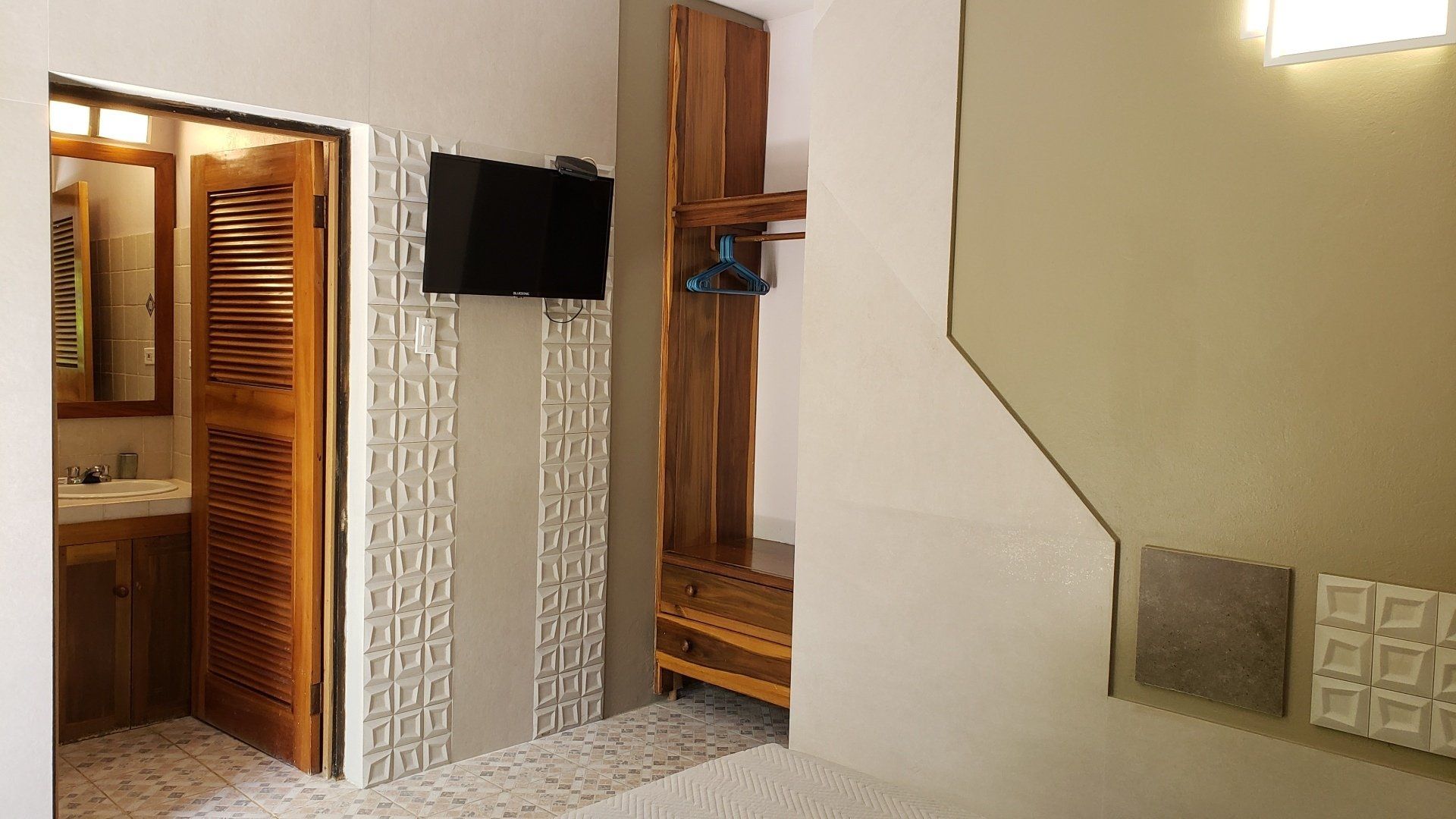 Hotel room interior with TV, closet, bathroom door, and light-colored walls and floor.