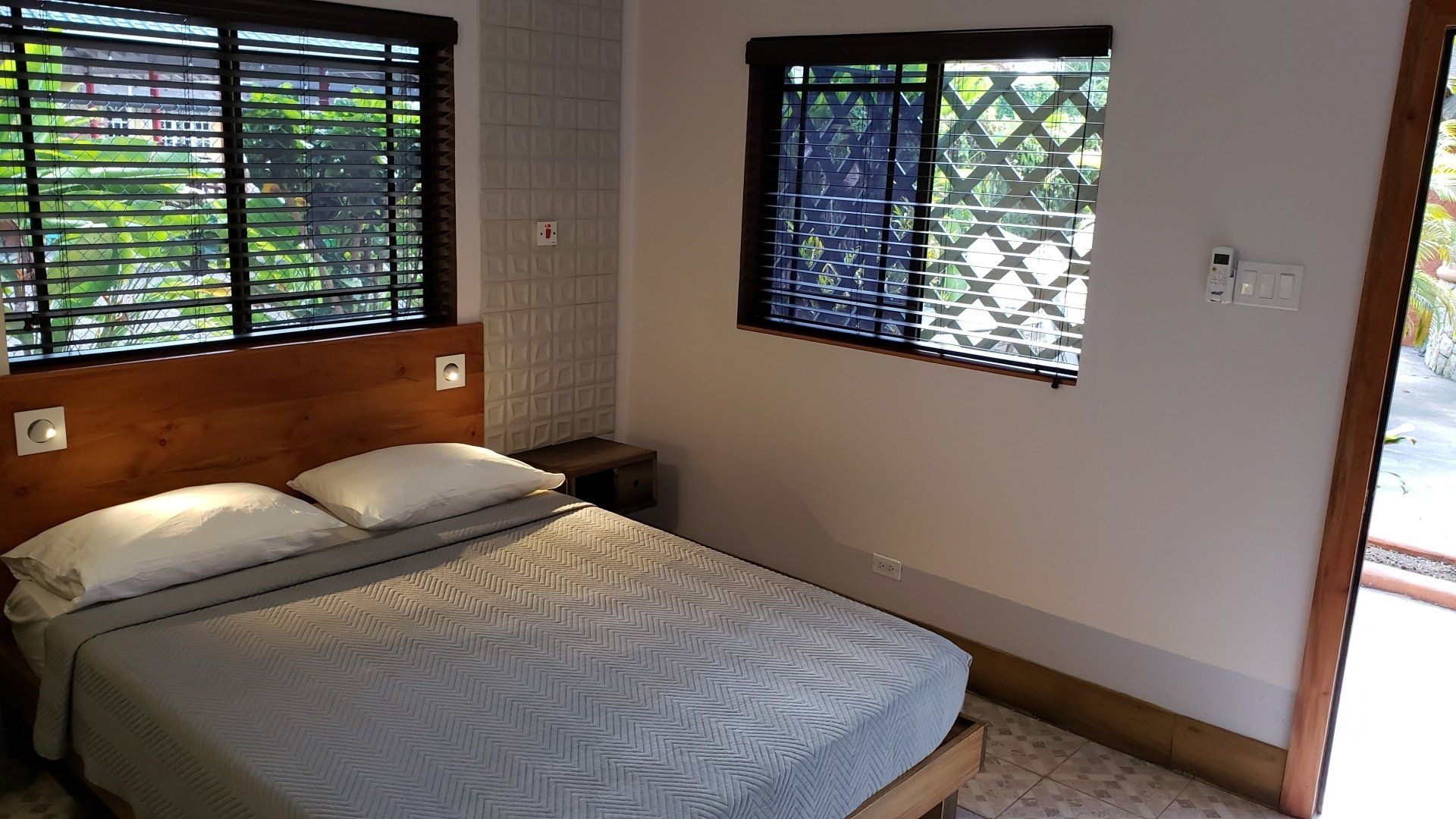 Bedroom with a double bed, two windows with blinds, and a nightstand.