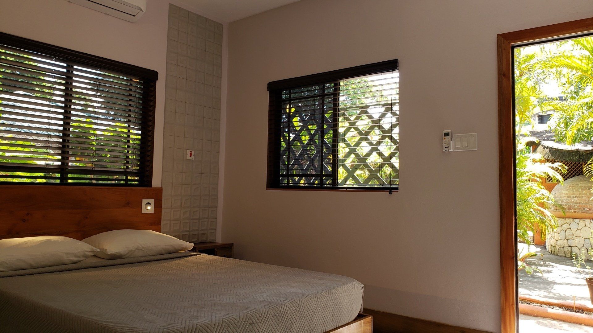 Bedroom with bed, windows with blinds, and open door to an outdoor garden.