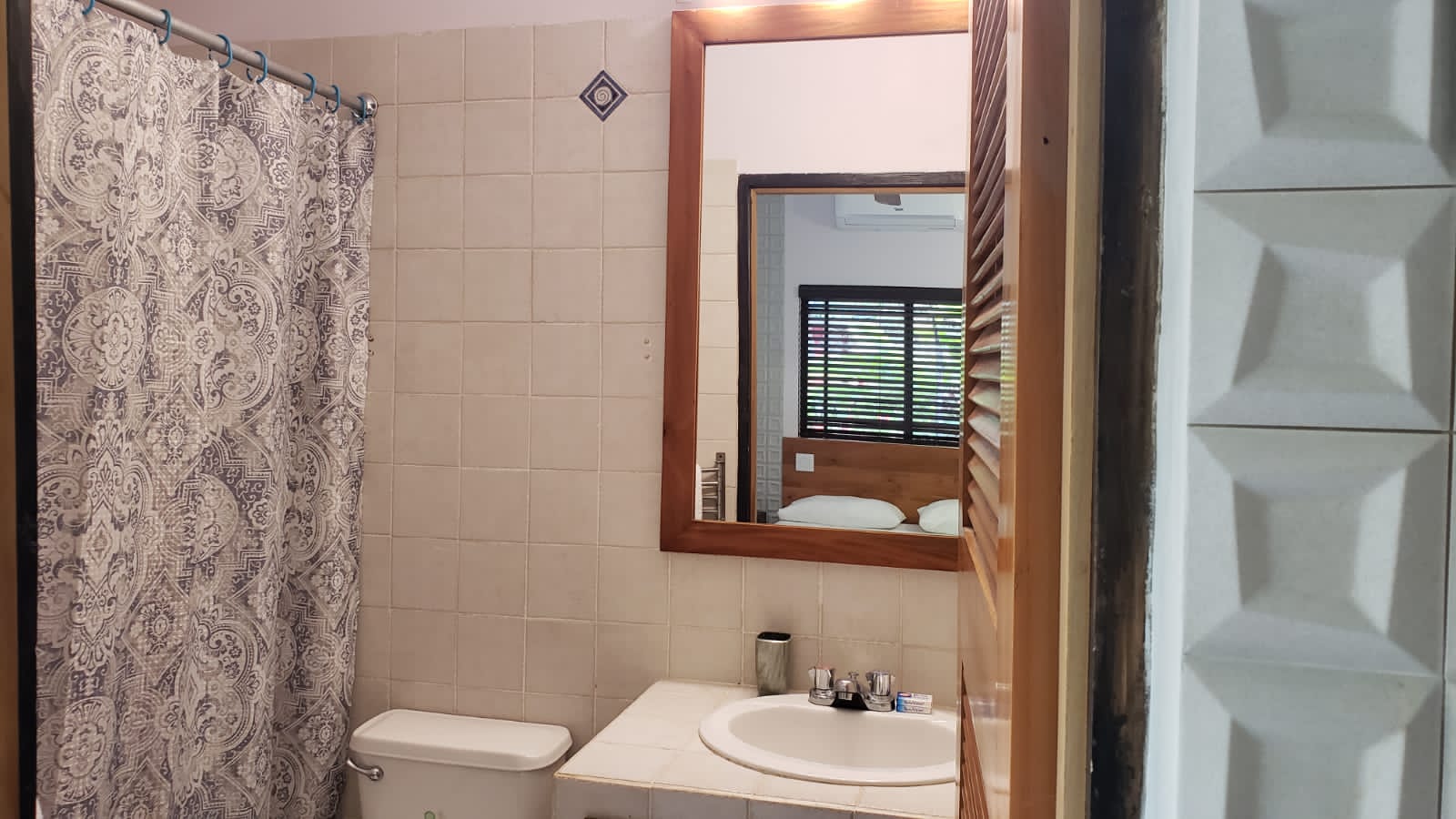 Bathroom with tiled walls, toilet, sink, mirror, and patterned shower curtain.