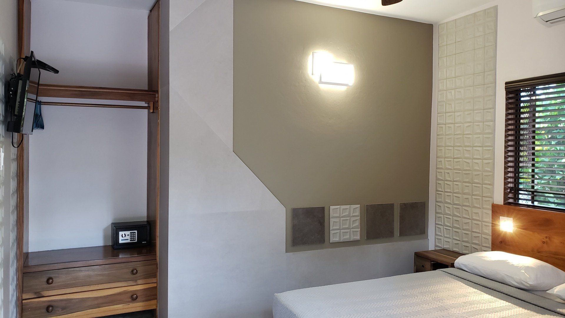 Bedroom with bed, closet, and window; neutral walls, wooden accents, safe.