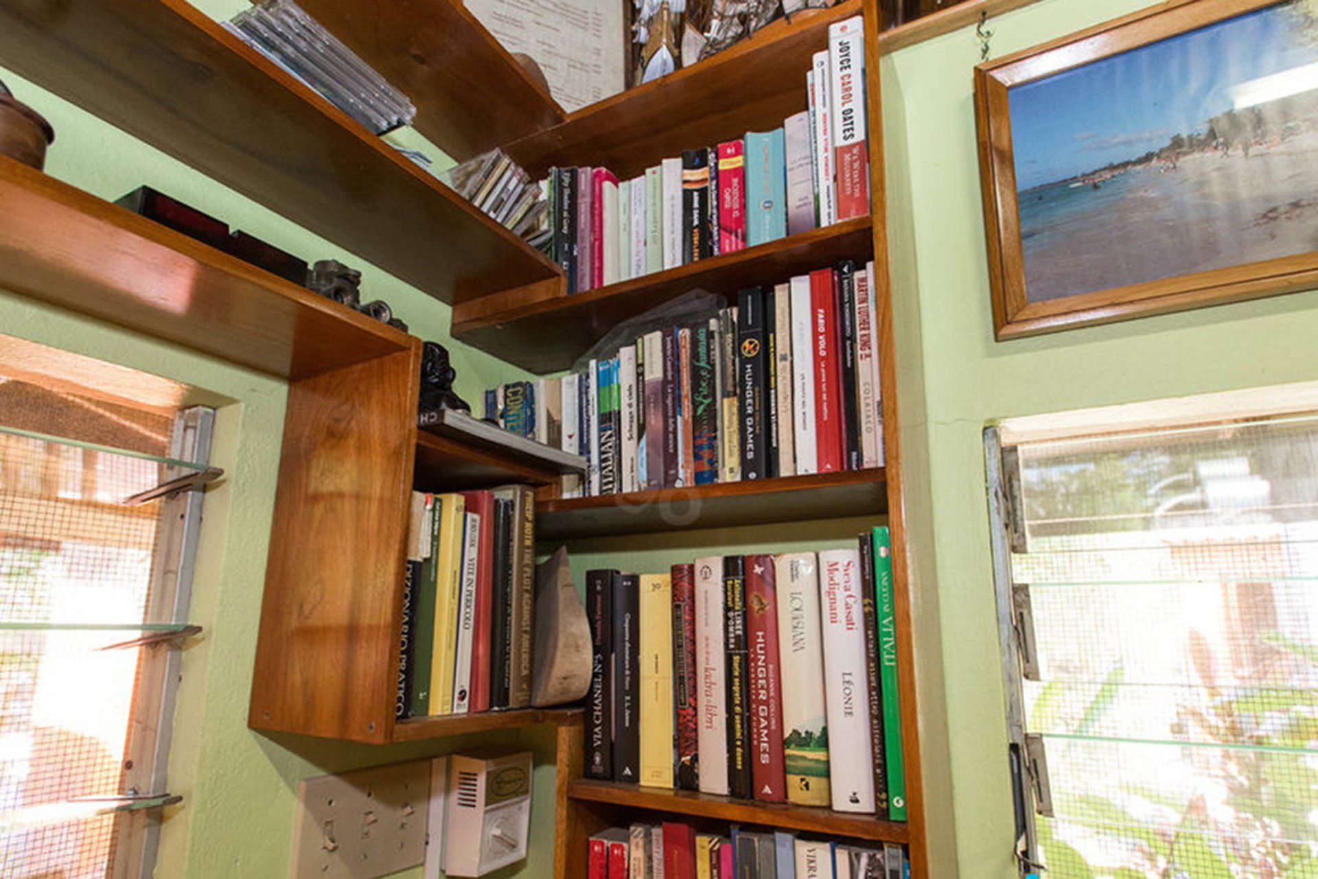 Wooden bookshelves filled with books in a corner of a room, next to a window with a picture frame on the wall.