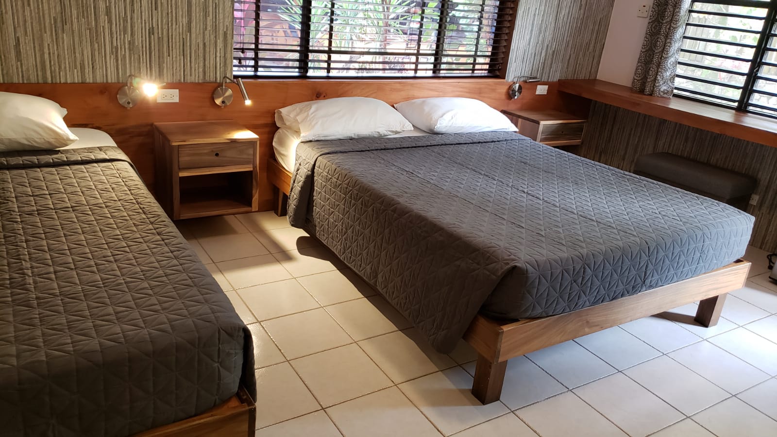 Bedroom with two beds, gray comforters, wooden furniture, and windows with blinds.