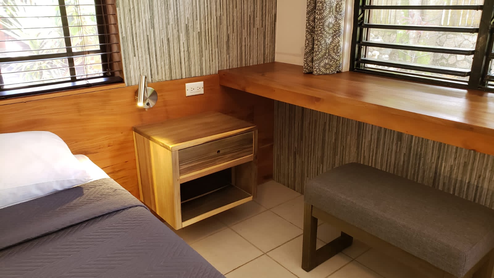 Cozy bedroom corner with a bed, nightstand, desk, and stool. Natural wood and neutral tones.