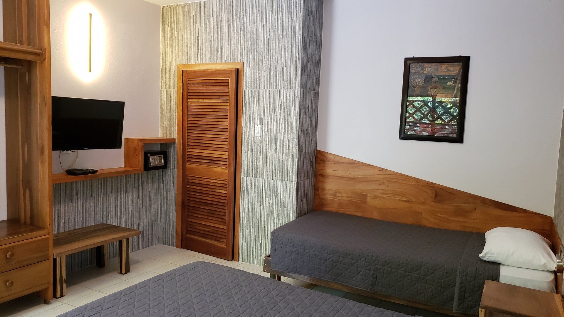 Bedroom with a single bed, wooden furniture, stone wall, TV, small safe, and framed artwork.