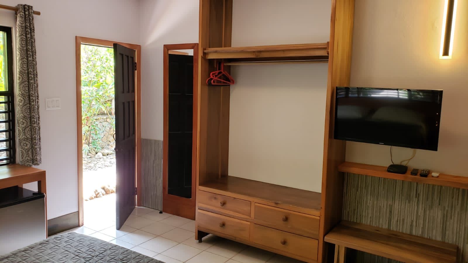 A room with wooden wardrobe and TV. Open door reveals outdoor view.