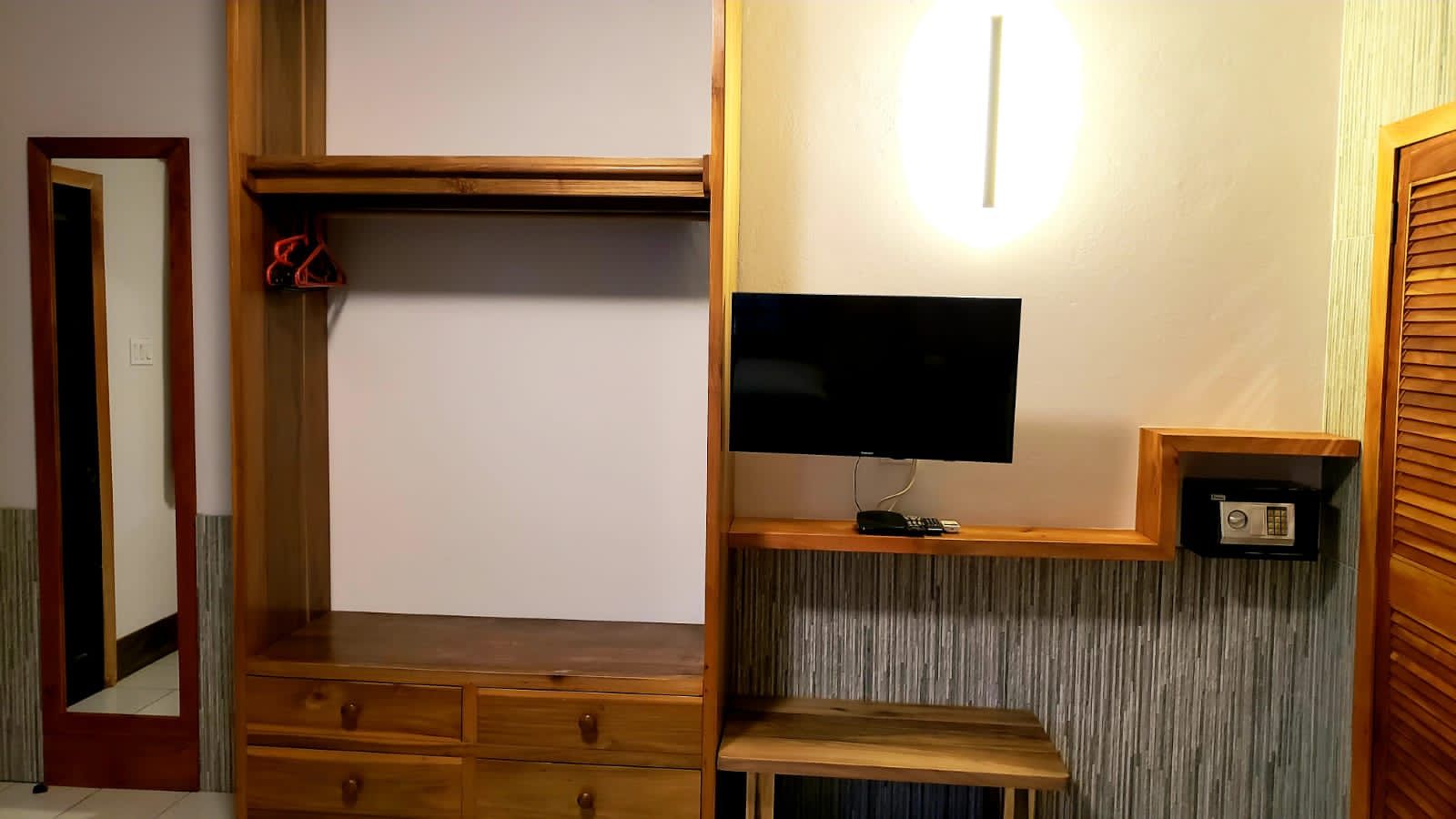 Wooden closet unit with mirror, drawers, TV, and safe; a small wooden desk is on the bottom.