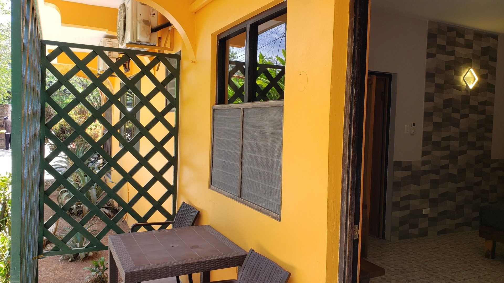 Outdoor patio with a table, chairs, and trellis next to a window and doorway.