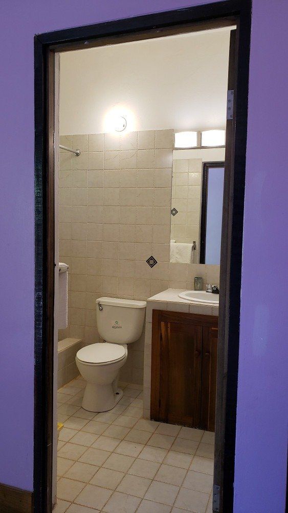 Bathroom interior, viewed through doorway. Includes toilet, sink, mirror, shower, and tiled walls.