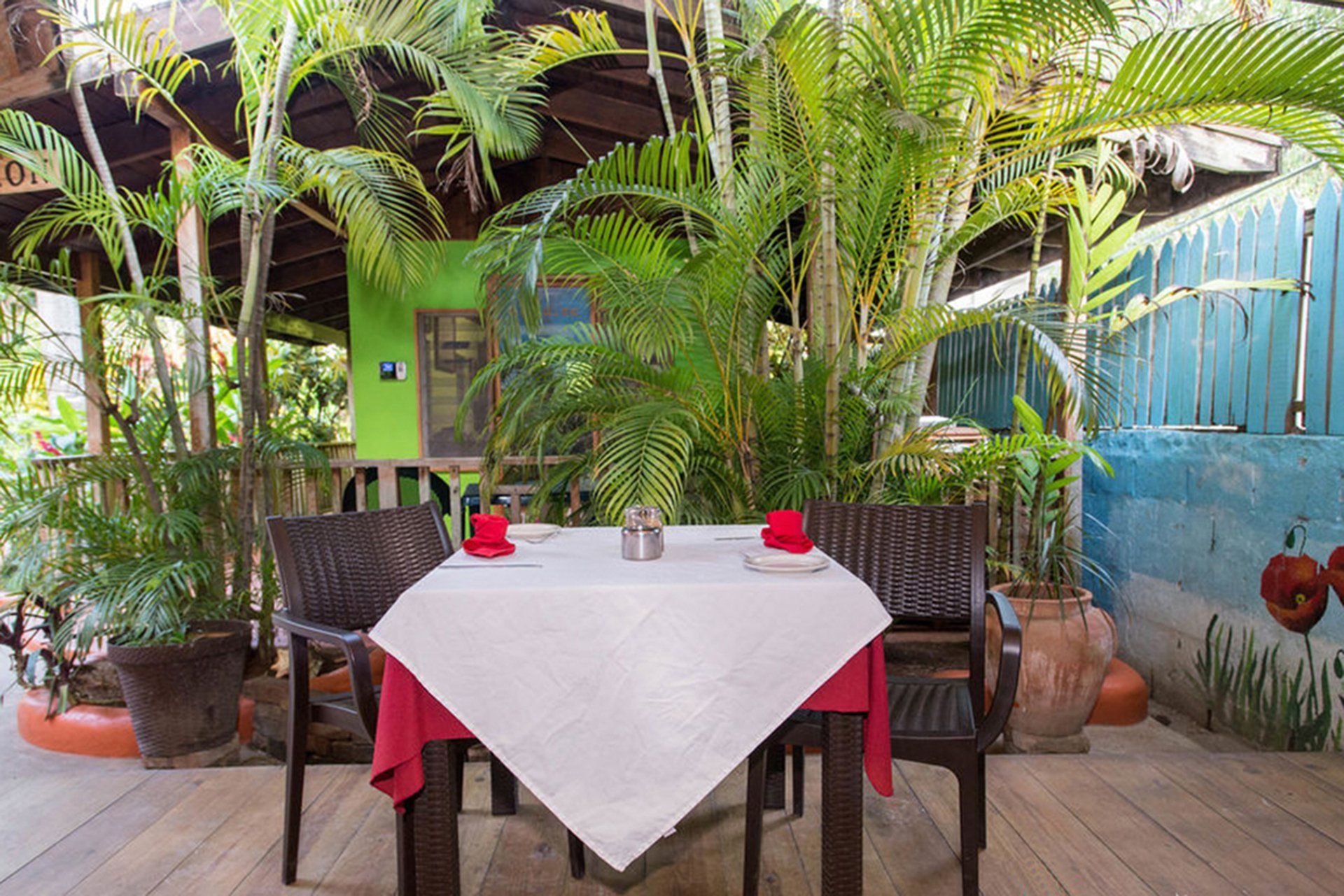 Outdoor restaurant table set for two, under greenery and wooden structure.