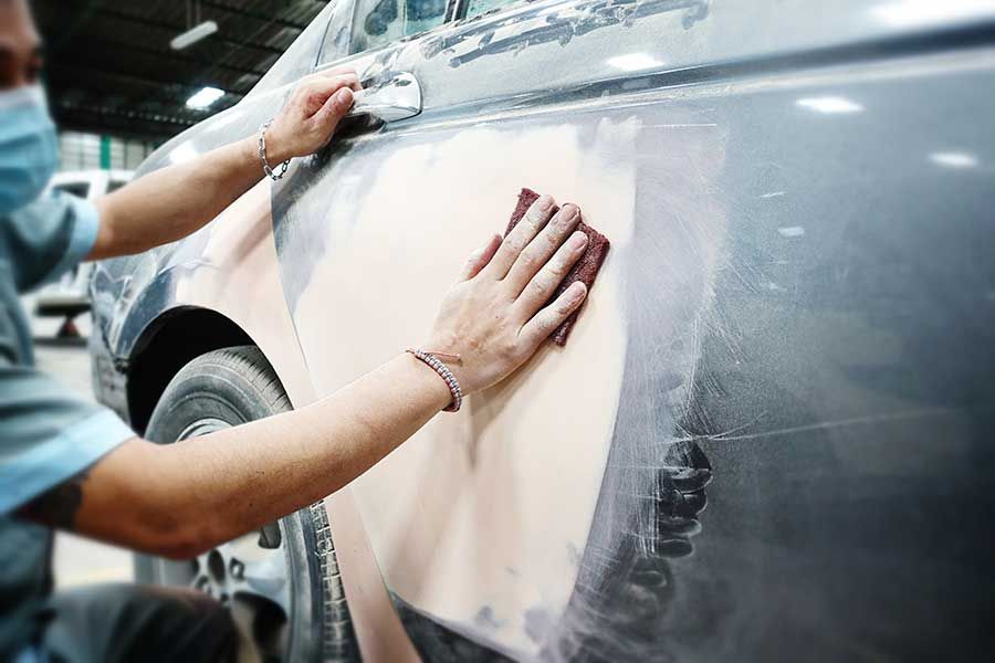 Auto body technician sanding repaired panel to smooth surface during collision prep and refinishing.