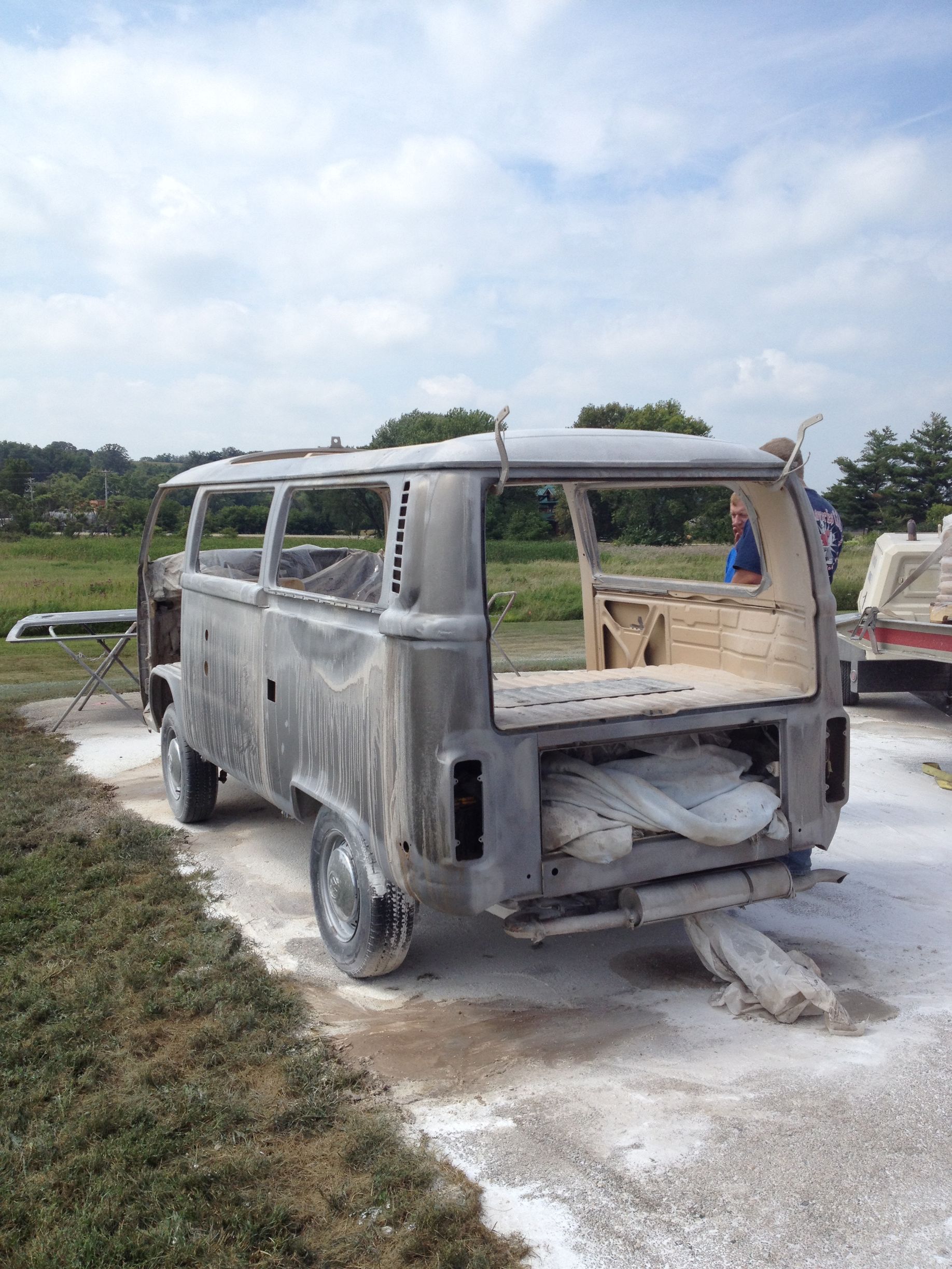 Stripped Volkswagen bus undergoing restoration outdoors with sanded body and exposed interior.