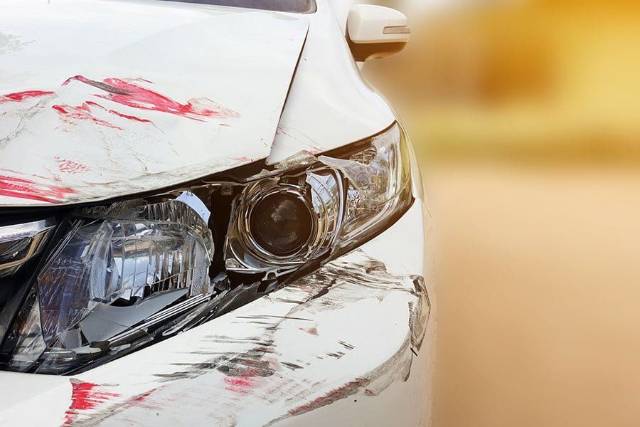White car with front-end collision damage and red paint transfer on bumper and fender.